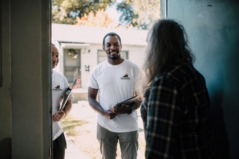 Purpose 417 team members in branded shirts speaking with a resident at their front door